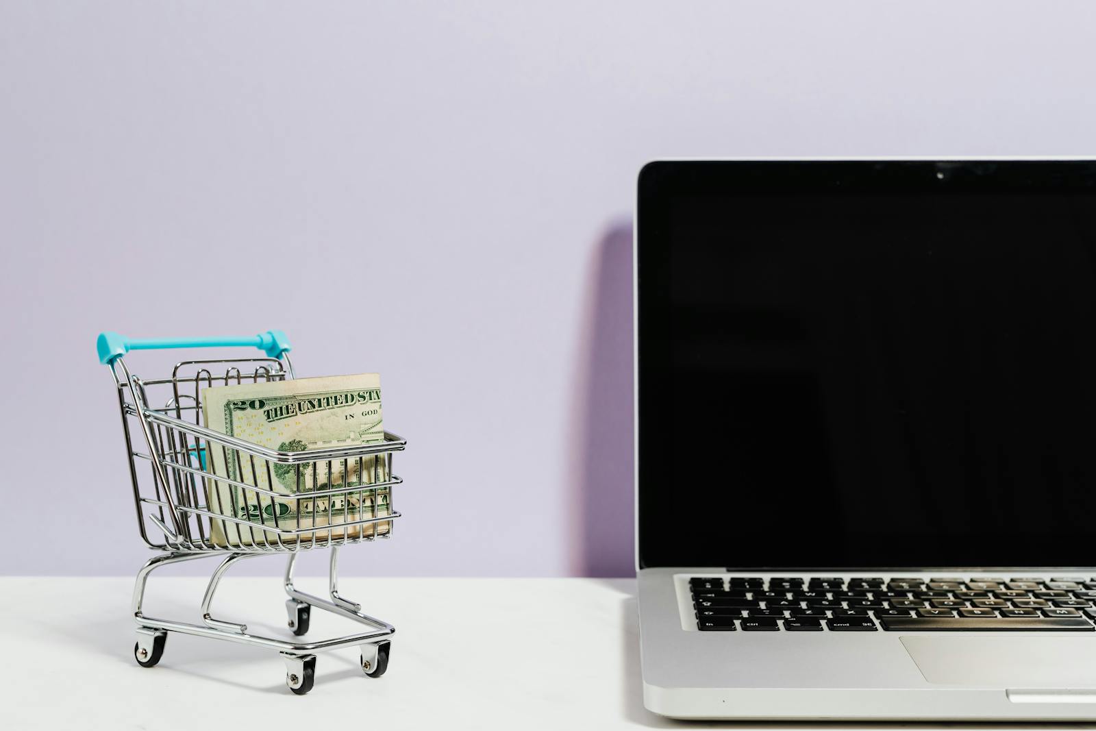 Shopping cart with money next to a laptop symbolizing online shopping and e-commerce.